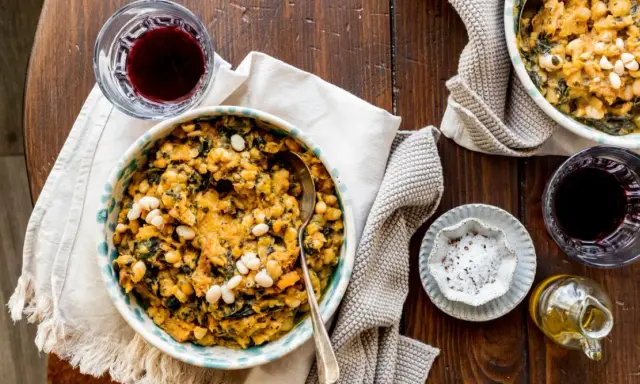 Un piatto fumante di fagioli e verdure, un classico delle ricette toscane, accompagnato da vino rosso e olio d'oliva.