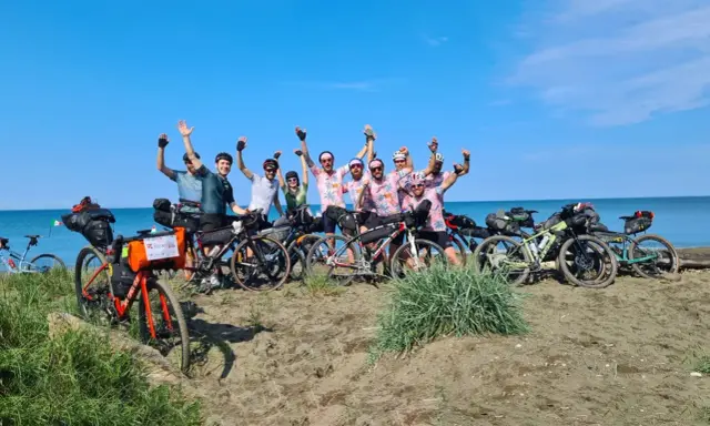 Un gruppo di ciclisti festeggia sulla spiaggia, pronti per un'avventura di cicloturismo in Toscana.