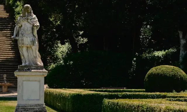 Statua romana domina la scalinata nei **Horti Leonini**. Giardini curati e alberi ombrosi creano un'atmosfera regale.