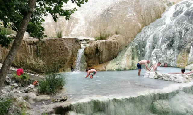 Persone si rilassano nelle piscine termali naturali di Castiglione d'Orcia, con cascate che scendono da rocce bianche.