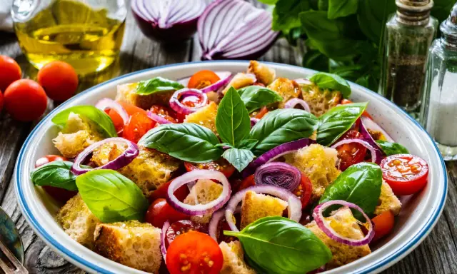 Panzanella ricetta: un'insalata estiva con pane raffermo, pomodorini, cipolla rossa e basilico fresco, condita con olio d'oliva.