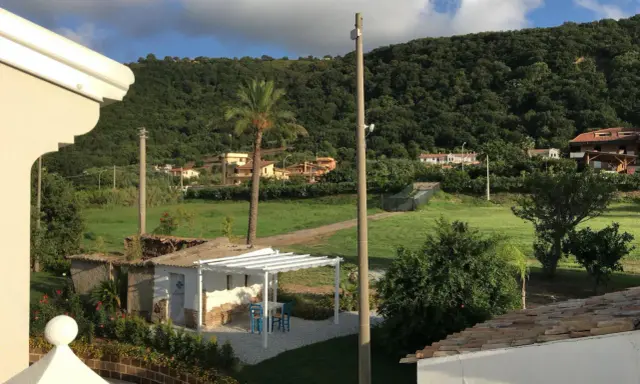 Un angolo di pace tra gli agriturismi in Calabria. Un pergolato bianco con tavolino e sedie blu, circondato da verde e colline rigogliose.