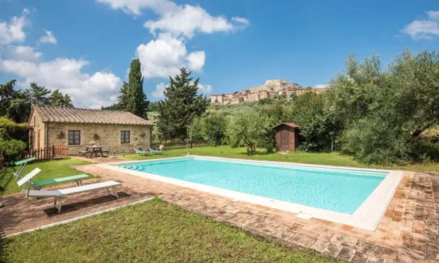Piscina in un casale in pietra nel Val d'Orcia, Italia, con un borgo medievale sullo sfondo.