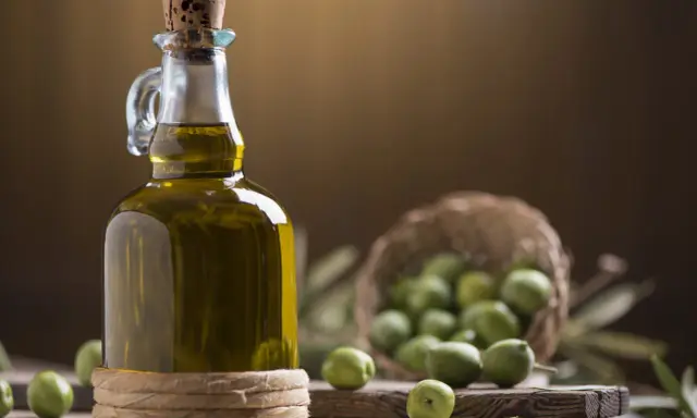 Bottiglia di olio extravergine di oliva, con olive verdi in cestino e su tagliere. La differenza tra olio di oliva e extravergine è la qualità.