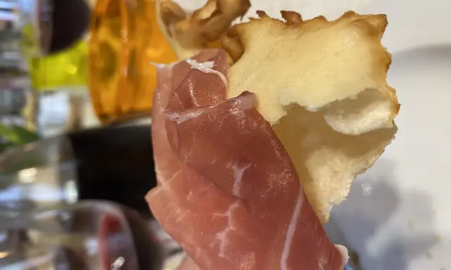 Fetta di gnocco fritto con prosciutto crudo, un classico dei piatti tipici Parma, accompagnato da vino rosso.