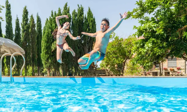 Bambini che saltano in piscina, una gioiosa Pasqua in Toscana tra cipressi e sole.