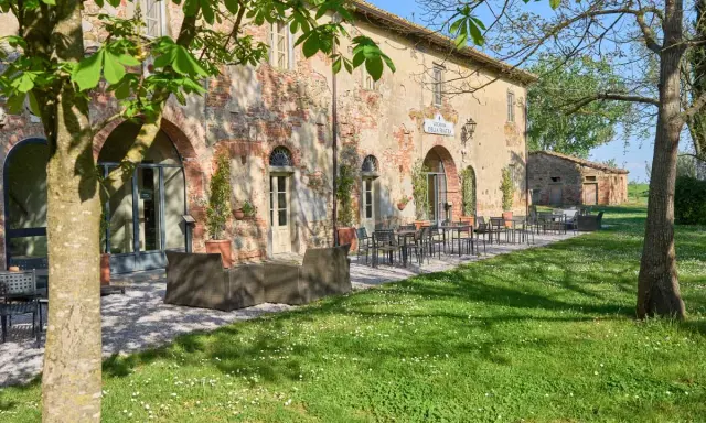 Antica locanda nel Val di Chiana, con tavoli all'aperto e un prato fiorito.