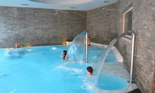 Bambini si divertono sotto cascate d'acqua in una piscina interna, un'ottima spa per famiglie in Lombardia.