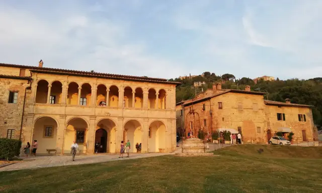 Edificio storico con portico ad archi, un pozzo e persone che passeggiano. Un luogo che sembra uscito da uno dei tanti film girati a Montepulciano.