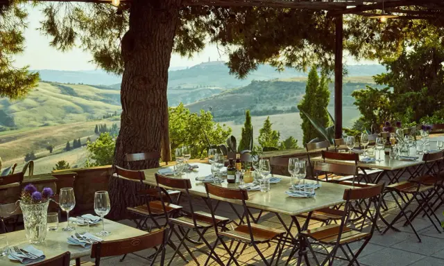 Tavoli apparecchiati sotto un pergolato con vista sulle colline toscane. Un'atmosfera perfetta per gustare i sapori degli agriturismi in Toscana.