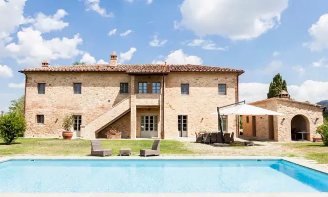 Splendida villa in pietra con piscina, un sogno di masserie toscane sotto un cielo azzurro.
