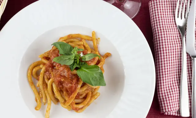 Pici al sugo, un classico della ricetta aglione Val di Chiana, serviti su un piatto bianco con basilico fresco.