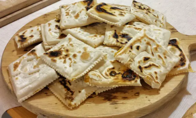 Piatto tipico cesenate: piadina fritta, dorata e leggermente bruciacchiata, servita su un tagliere di legno.