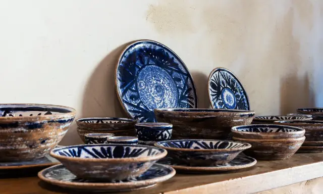 Ceramiche artigianato toscano con decori blu su fondo grezzo. Piatti e ciotole disposti su una mensola di legno.