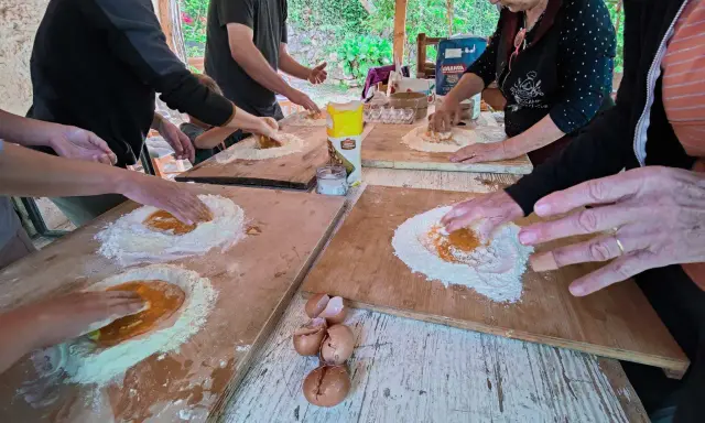 Bambini e adulti impastano farina e uova in una fattoria in Abruzzo, un'esperienza culinaria all'aperto.