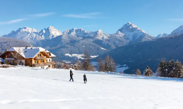 Un agriturismo con un gallo rosso sul tetto, immerso in un paesaggio innevato con montagne maestose.