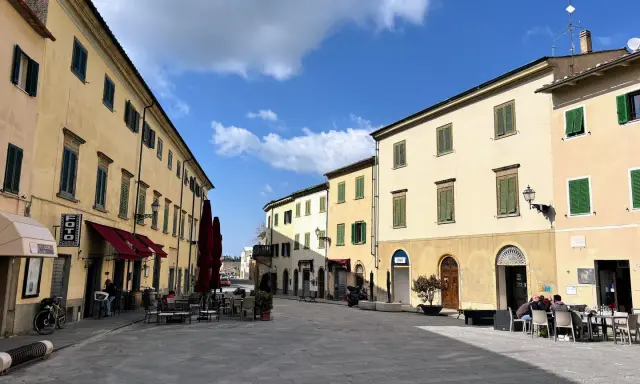Piazza soleggiata a Pomarance, con edifici storici, tavolini all'aperto e scorci suggestivi da scoprire.