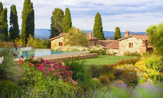 Vacanze in Toscana dove andare? Un casale in pietra con piscina, circondato da cipressi e un giardino fiorito.