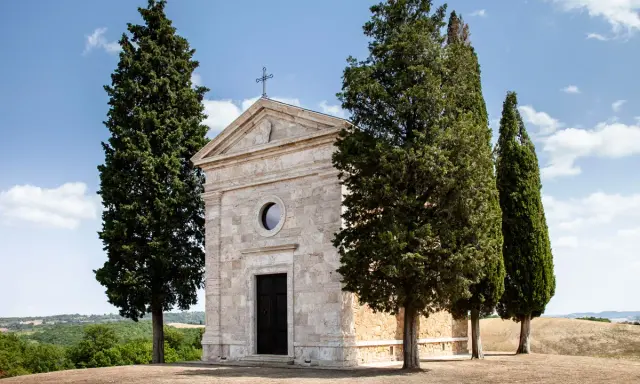 La chiesa di Vitaleta, con i suoi cipressi iconici, si erge solitaria su una collina toscana sotto un cielo azzurro.