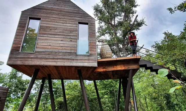 Un'esperienza unica per dormire nella natura toscana: una casa sull'albero in legno, con una persona che ammira il paesaggio dalla terrazza.
