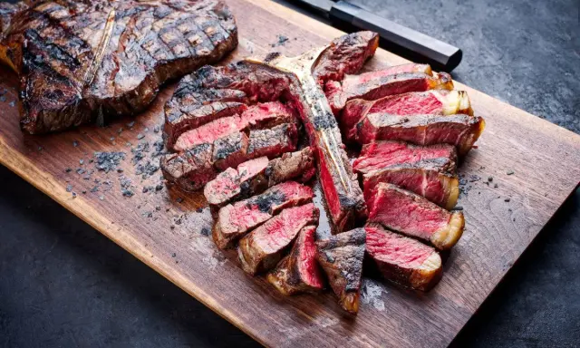 Una succulenta fiorentina alla griglia, affettata e servita su un tagliere di legno, con sale grosso sparso.