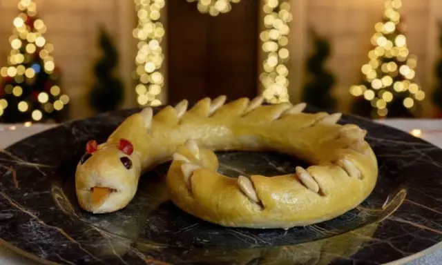 Dolci tipici Perugia: un serpente di pasta frolla dorata, con occhi rossi e lingua arancione, adagiato su un piatto scuro.