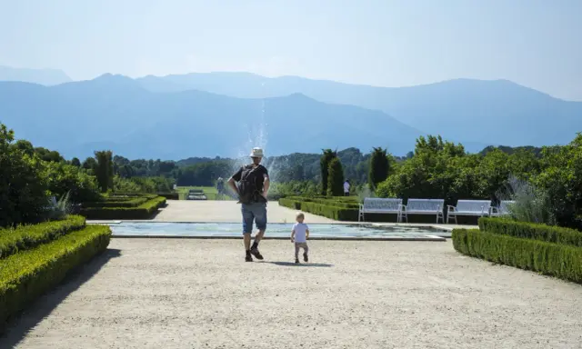 Un uomo e un bambino passeggiano in un giardino curato, con fontane e montagne sullo sfondo. Una giornata perfetta in Piemonte con bambini.