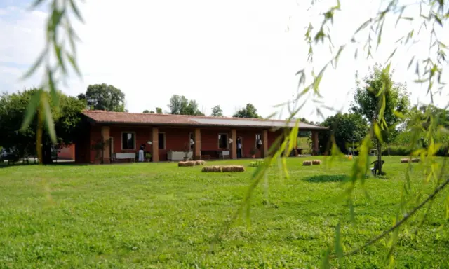 Un'accogliente fattoria didattica alle Fornaci, con un edificio rosso, balle di fieno e un prato verde.