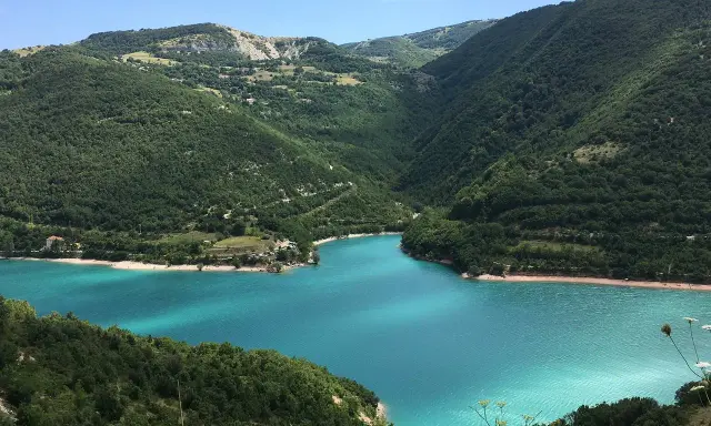 Un lago turchese incastonato tra colline verdi, ideale per il trekking nelle Marche.