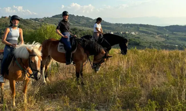 Tre ragazze in sella a cavalli godono di splendide passeggiate a cavallo in Abruzzo, tra colline verdi e cielo azzurro.