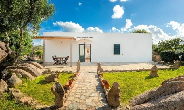 Un sentiero in pietra conduce a un bianco casolare, circondato da rocce granitiche e vegetazione mediterranea. Ideale per scoprire gli agriturismi Sardegna nord.