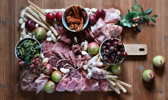 Tagliere con salumi tipici lombardi, frutta, sottaceti e grissini su un tavolo di legno.