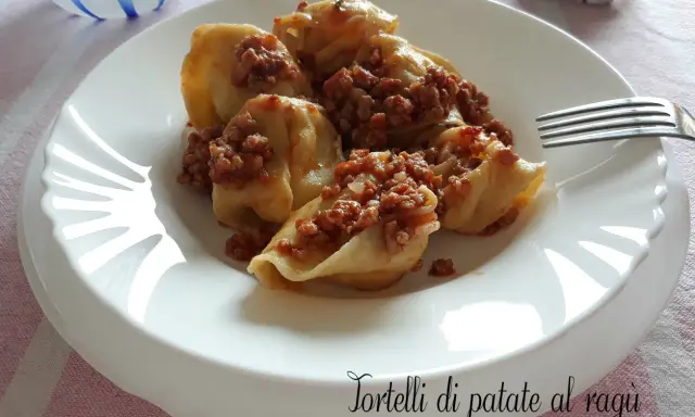 Tortelli di patate al ragù, un piatto gustoso e confortante, servito su un piatto bianco con una forchetta.