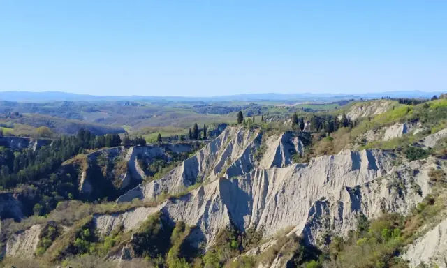 Paesaggio lunare con calanchi toscana, creste erose e vegetazione verdeggiante sotto un cielo azzurro.