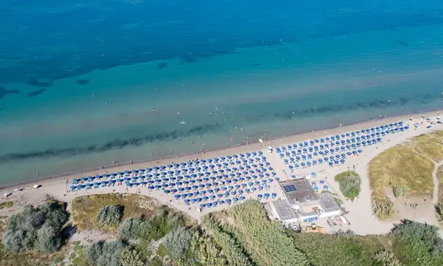 Spiaggia attrezzata con ombrelloni blu, ideale per campeggi in Toscana sul mare per bambini. Acqua cristallina e gente che si gode il sole.