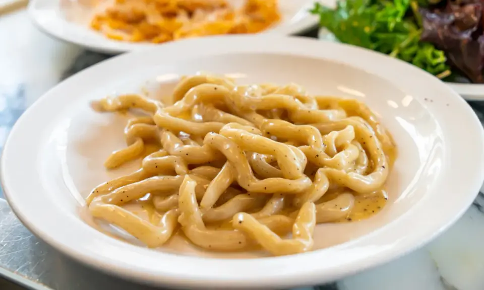 Pici cacio e pepe, un classico tra i piatti tipici di Siena, serviti su un piatto bianco.