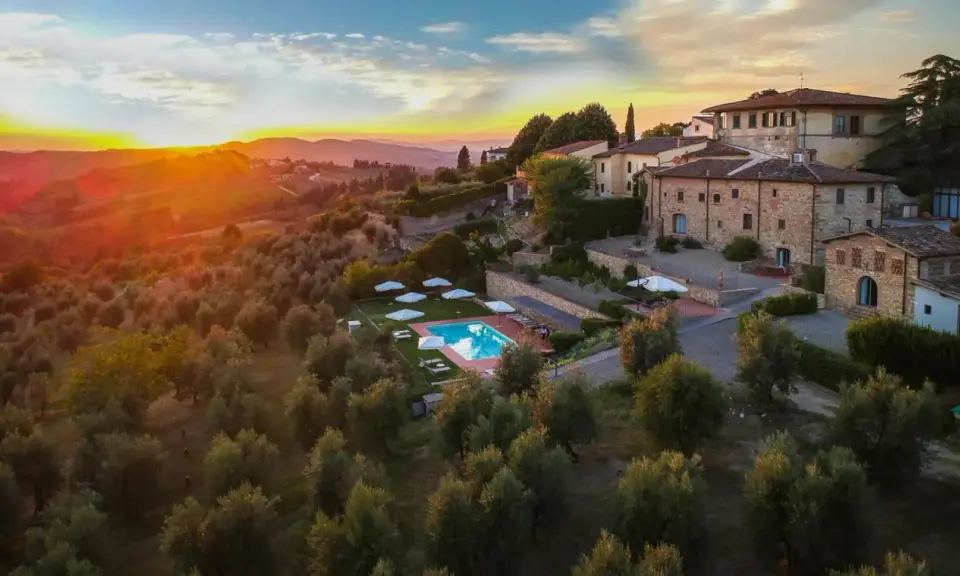 Un tramonto dorato illumina un agriturismo con piscina, immerso tra ulivi e colline, perfetto per un tour della Toscana.