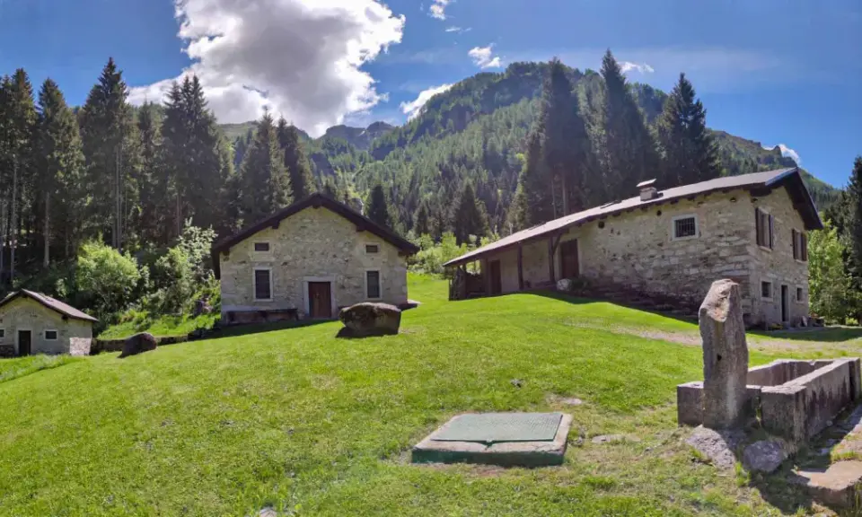 Agriturismi lombardia montagna: casette in pietra immerse nel verde, con boschi e montagne sullo sfondo.