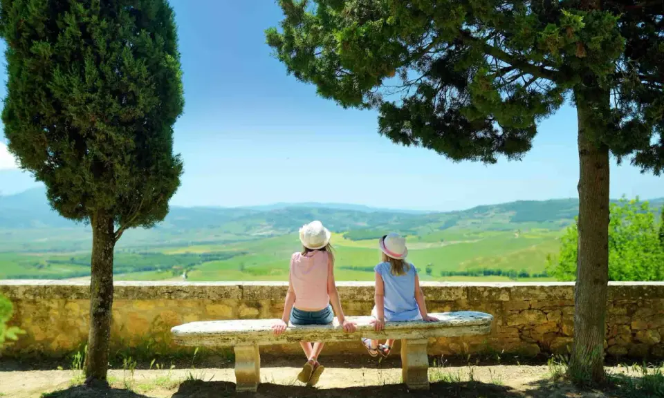 Due bambine con cappello ammirano il panorama collinare toscano, un perfetto weekend con bambini in Toscana.