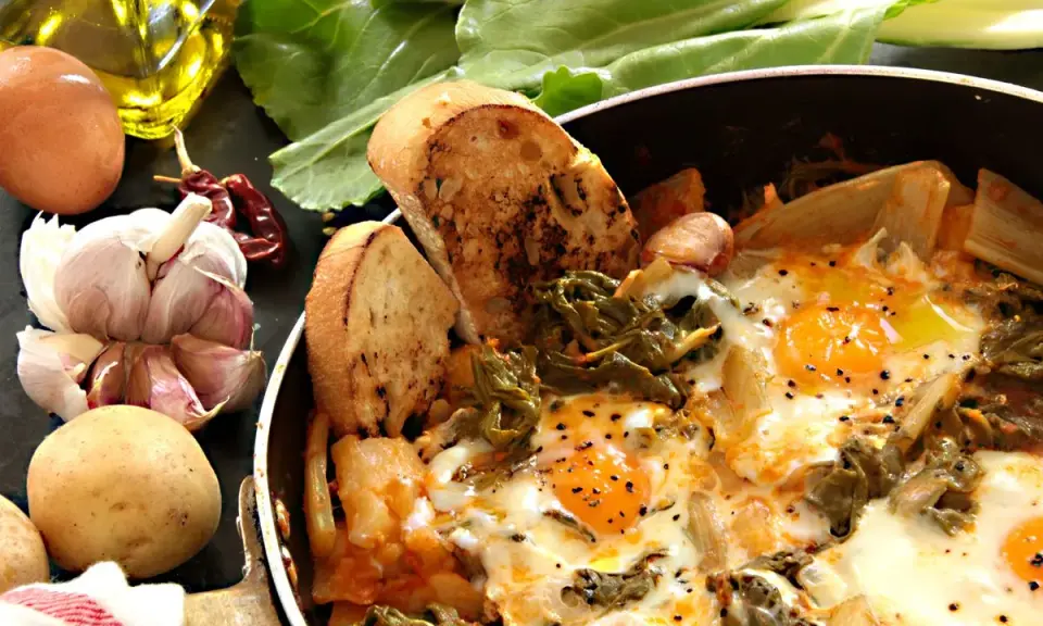 Uova cotte in padella con verdure, patate, aglio, peperoncino e pane tostato. Un piatto rustico e saporito, perfetto per una colazione o un pasto veloce.