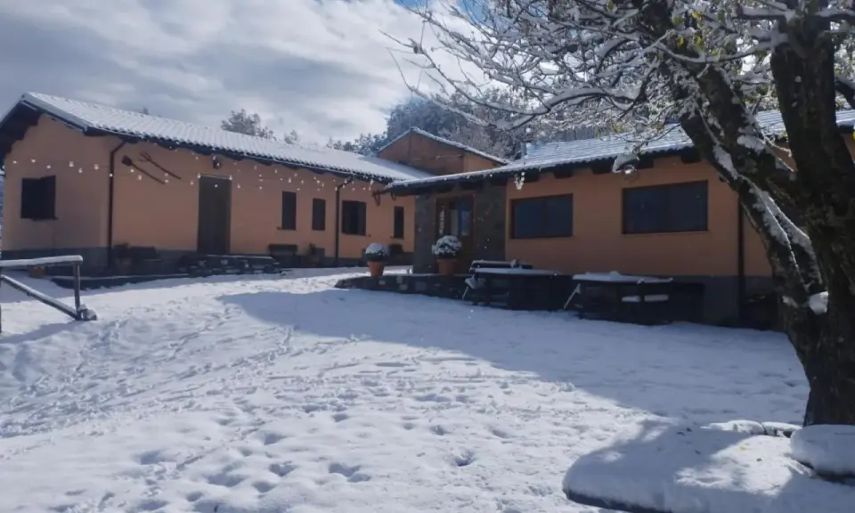 Agriturismo Acqua Bianca imbiancato dalla neve. Un paesaggio invernale incantevole con edifici color pesca e un cielo azzurro con nuvole bianche.
