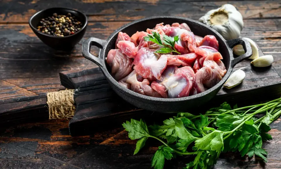 Piatto toscano con interiora di pollo crude in padella, con aglio, pepe e prezzemolo su tagliere di legno scuro.