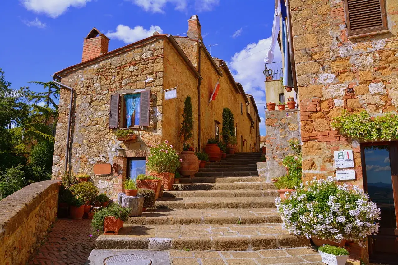Pienza cosa vedere: scalinata in pietra con vasi di fiori e case in tufo sotto un cielo azzurro.