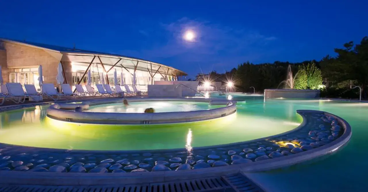 Piscine illuminate di notte a Chianciano Terme, con una luna piena nel cielo e persone che si rilassano nell'acqua calda.