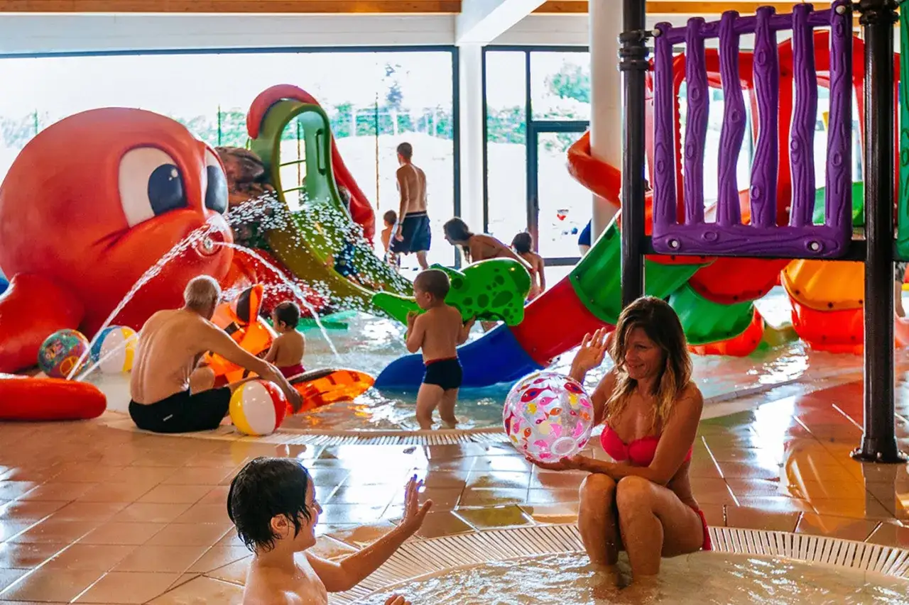 Bambini e adulti si divertono in una piscina con scivoli colorati e un grande polpo spruzzante. Un luogo ideale per una spa per bambini in Piemonte.