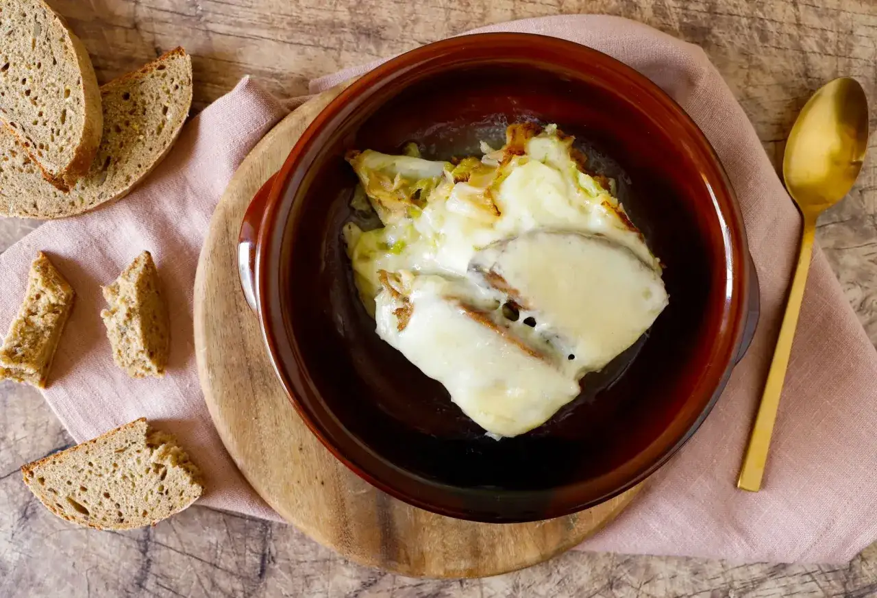 Piatto tipico valdostano: zuppa di pane e formaggio fuso, servita in ciotola con pane rustico a fette e cucchiaio dorato.