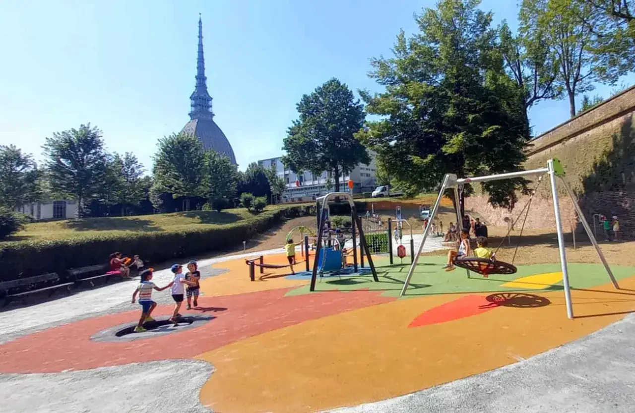 Un parco giochi colorato nel Piemonte con bambini che si divertono sull'altalena e sui giochi. In lontananza, la Mole Antonelliana.