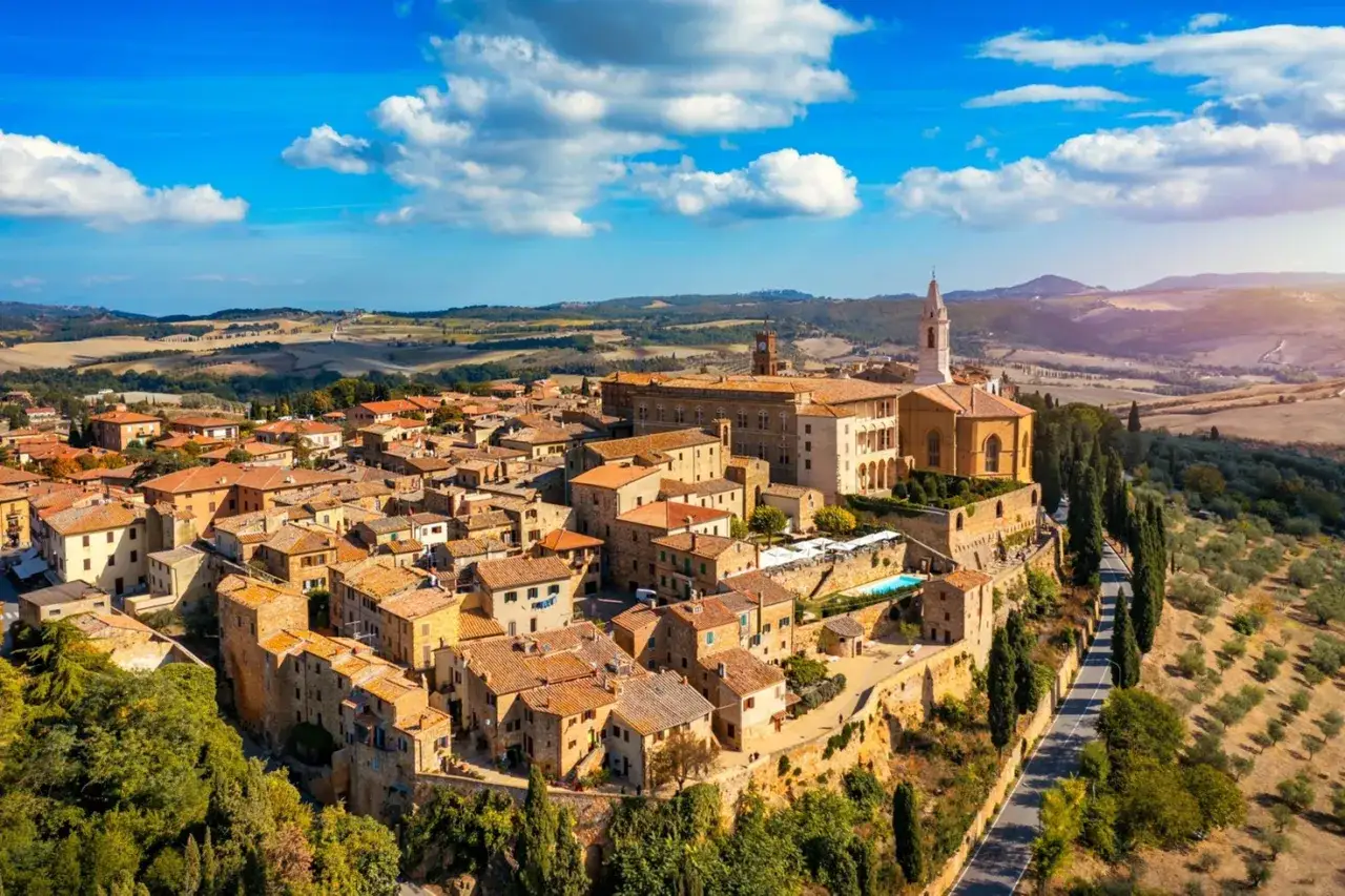 Vista aerea di un borgo medievale con tetti in terracotta, una chiesa imponente e colline ondulate, come in una Val d'Orcia mappa da sogno.