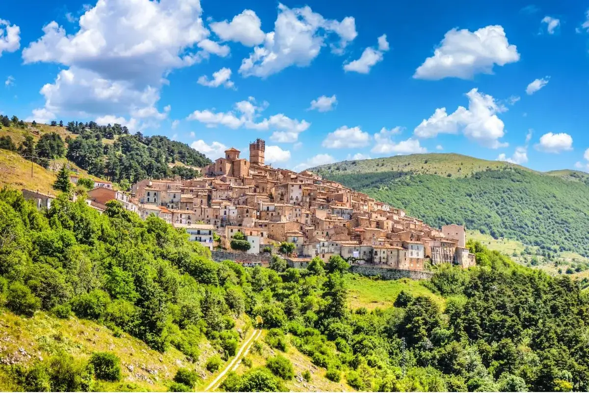 Borgo medievale arroccato sui monti dell'Abruzzo, con case in pietra e torri che si stagliano contro il cielo azzurro e nuvoloso.