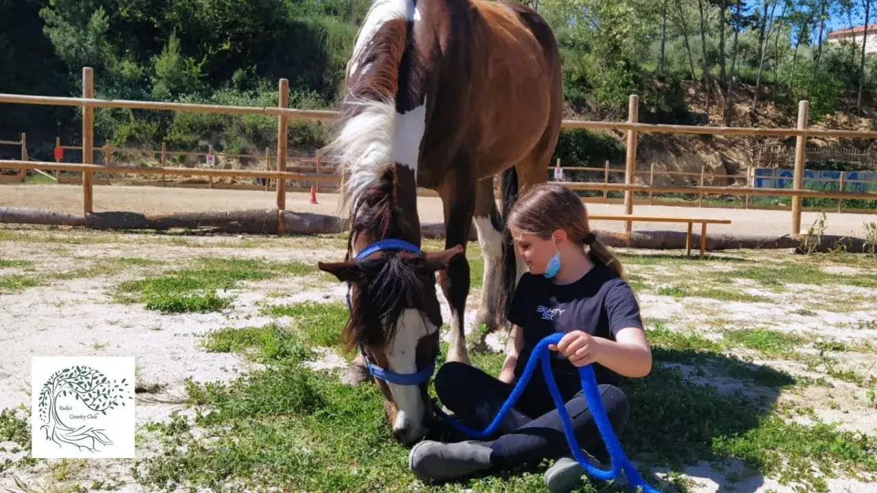 Bambini e cavalli in una fattoria in Abruzzo. Una bambina con una corda blu accarezza un cavallo.
